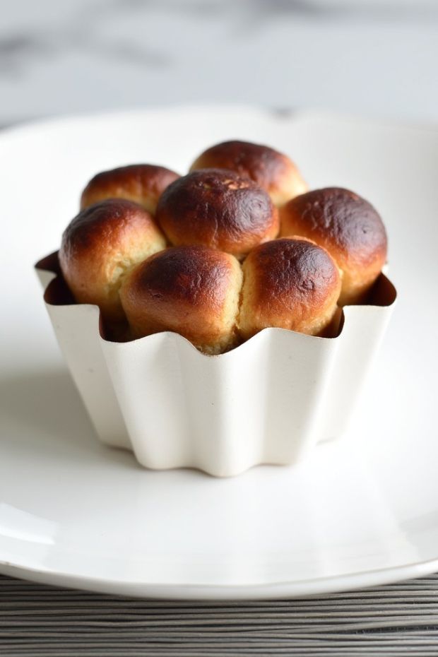 Golden brioche à tête rolls, soft and buttery French pastry in a fluted dish on a sleek white plate.