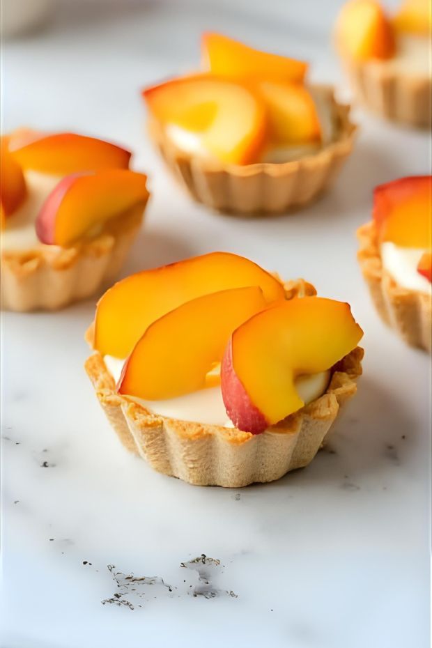 Colorful Peach Vanilla Bean Custard Tarts topped with fresh peach slices on a marble surface.